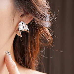 Close-up of a silver-tone liquid metal C-shaped earring worn on a model's ear