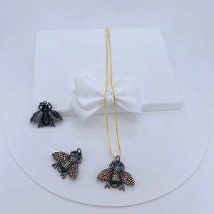 Detailed view of bee pendants in copper with inlaid zirconias on a gold chain necklace