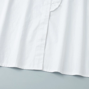 Detail of white cotton shirt hem with ruffled decorative elements and clean stitching