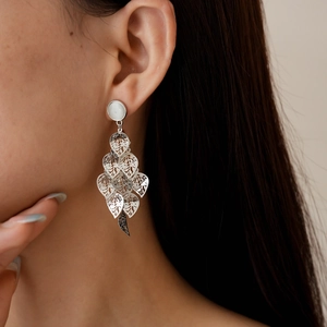 Close-up of dangling silver leaf drop earrings with hollow metal design on model