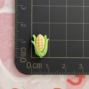 Detailed close-up of a 1.5 cm resin corn charm with size measurements on a scale