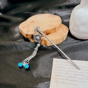 Detailed shot of a silver hair pin with hollow floral pattern and turquoise tassel beads