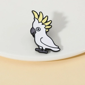 Détail d'une broche perroquet en émail avec huppe jaune sur une assiette blanche
