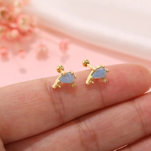 Macro view of mini gold sea-themed screw back earring with light blue stone on fingertip