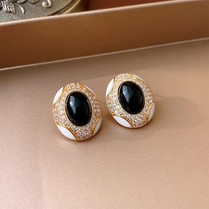 Close-up of vintage black oval gemstone earrings with white enamel and pavé rhinestones