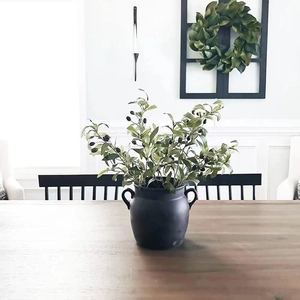 Close-up of artificial olive branches in a matte black ceramic vase on a wooden table
