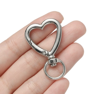 Macro detail of silver heart-shaped swivel lobster clasp held by hand on white background