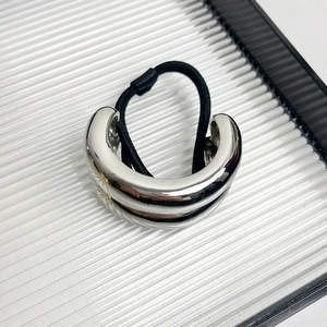 Detail of silver arched metal buckle on black hair tie against textured background