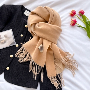 Close-up of thick camel cashmere-like tassel scarf layered on a black tweed jacket