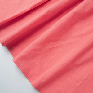 Detailed close-up of coral pink cotton linen fabric with natural slub texture and neat stitching