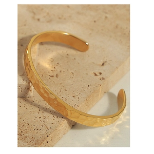 Dettaglio della texture martellata sul bracciale a polsino in acciaio dorato su pietra