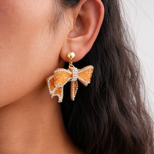 Close-up of amber resin bow earrings with orange rhinestones on model's ear