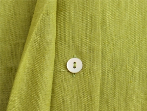 Dettaglio macro del tessuto in lino verde erba con un bottone in madreperla bianca sul capo