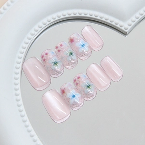 Pink cat-eye press-on nails with blue floral art and glitter finish displayed on mirror