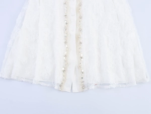 Detailed close-up of white dress lace hem with 3D flower embroidery and pearl sequins