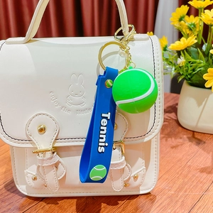 Mini tennis ball keychain with blue silicone strap and gold ring on a white stylish bag