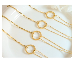 Detail of minimalist gold chain link bracelet with ring pendant on a white ceramic plate