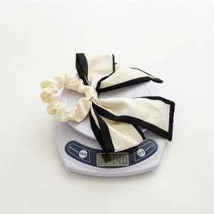 Detail shot of a beige bow hair scrunchie with black trim on a digital scale weighing 14g