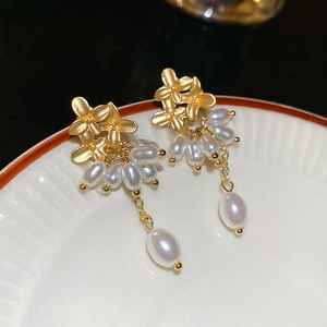Close-up of golden flower earrings with white baroque pearl tassels on a ceramic plate