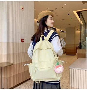 Detailed back view of a light yellow casual school backpack with a pink cartoon charm