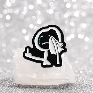 Detailed close-up of a funny black and white cartoon stickman enamel pin on crystal stone