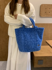 Borsa tote blu in peluche indossata da una modella con maglieria bianca in un interno