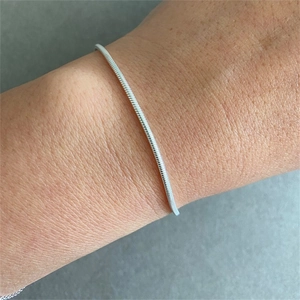 Macro close-up of a slim silver snake bone chain bracelet worn on a female wrist