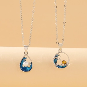 Close-up of ocean wave pendants with blue enamel, white pearl, and sunset engraving details