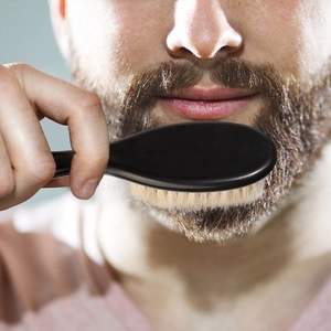 Men's beard brush with soft bristles and black handle used for grooming facial hair