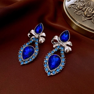 Detail of silver bow and blue teardrop crystal earrings on luxury silk fabric