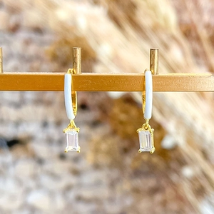 Detail of gold hoop earrings featuring white enamel and baguette-cut crystal drop