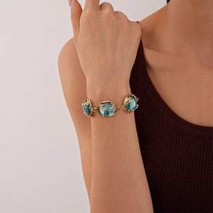 Detailed close-up of a gold bracelet featuring light blue resin stones and leaf carvings