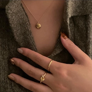 Close-up of a 925 silver key necklace and minimalist rings on a dark green knit background
