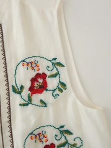 Détail de la broderie florale sur un gilet en satin blanc avec fleurs rouges et feuilles