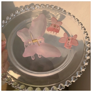 Detailed view of three frosted pink butterfly hair claws on a glass tray in soft light