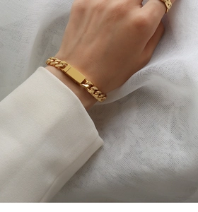Close-up of gold-plated Cuban chain bracelet with ID plate and matching ring on model