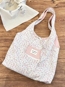 Floral canvas tote bag with pink plaid pocket and lace detail on a warm wooden floor