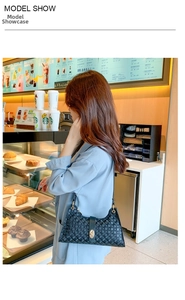 Model wearing a black embossed underarm bag with gold metal buckle and circle patterns