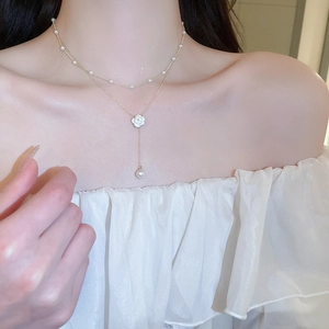 Close-up of double-layered gold necklace with camellia flower pendant and pearls on model