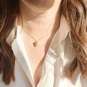 Detail of a gold heart locket necklace with red birthstone on a model with white shirt