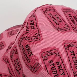 Detailed macro of pink canvas hat fabric featuring tickets and NECY STUDIO printing