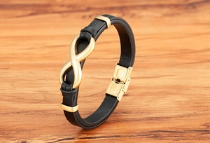 Detail of infinity symbol charm on black leather braided bracelet with gold metal buckle