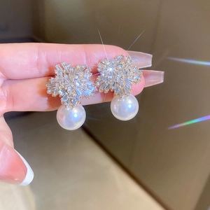 Elegant gold flower earrings with sparkling zircons and white pearls shown on fingers