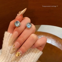 Detailed close-up of light blue crystal tassel earrings held by a model with a knit sweater