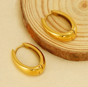 Gros plan de boucles d'oreilles créoles ovales en acier doré avec finition polie et fermoir