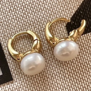 Detailed view of elegant gold hoop earrings with large round white pearls on a textured background