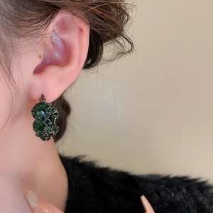 Close-up of vintage-style double-ring earrings featuring deep green rhinestones and metal