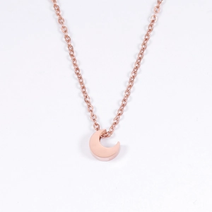 Gros plan d'un pendentif demi-lune en or rose poli sur une chaîne à mailles assortie