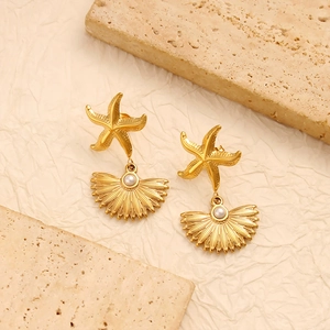 Gold starfish and shell pearl earrings displayed on natural beige stone background
