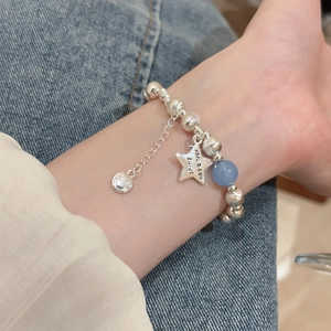 Star and smiley face charm bracelet with light blue bead shown on a denim background